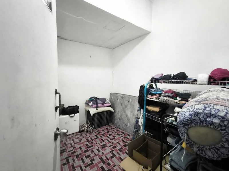 Room features: white painted walls, exposed ceiling, pink and grey tiled flooring, metal shelving unit, mattress on the floor, stacked boxes, clothing items on shelves, door leading to another space.