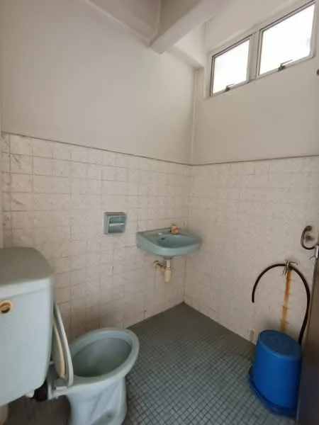 Bathroom features: white tiled walls, blue ceramic sink, toilet, shower with hose, small window, grey tiled flooring, wall-mounted toilet paper holder, blue bucket.