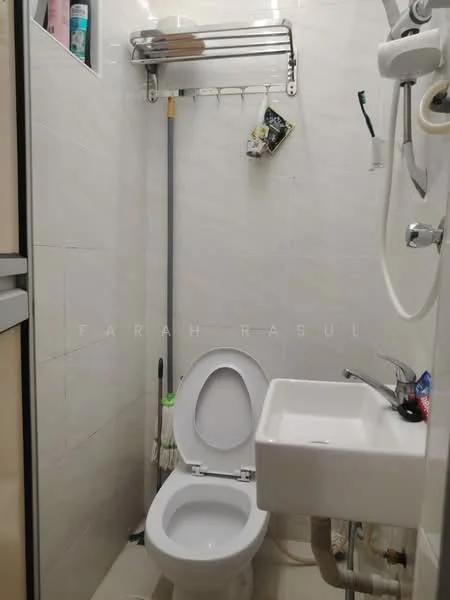 Bathroom features: white ceramic toilet, small white sink, chrome faucet, shower head, wall-mounted shower hose, tiled walls, tile flooring, mirror above sink, towel rack, cleaning supplies on wall rack.