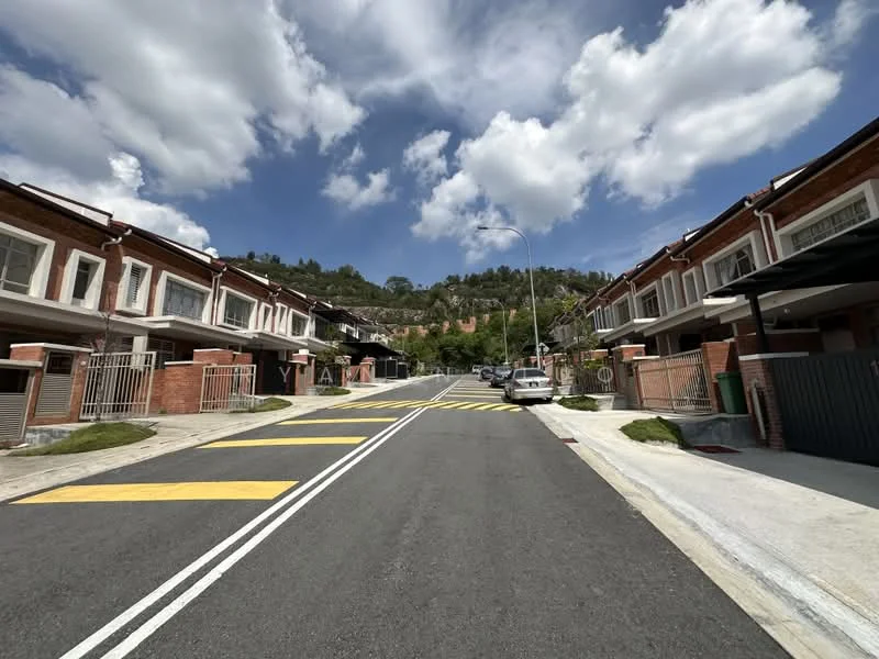 Exterior type: linked terrace house; features: two-storey linked terrace houses, brick facade with white trim, paved driveway, asphalt road, yellow road markings, street lighting, landscaped grass patches, surrounding hills in background, clear blue sky with clouds; style: modern.
