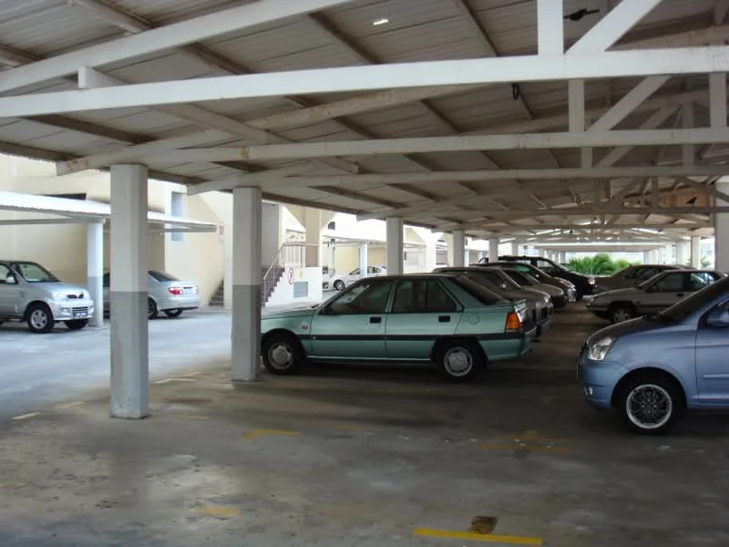 Exterior type: parking deck; features: covered parking, concrete flooring, metal roof, support columns, marked parking spaces, multiple vehicles visible, open-air structure, surrounding residential buildings; style: modern.