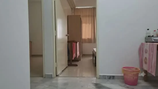 Room features: white painted walls, marble flooring, wooden wardrobe, curtains, door, basket, table, pink tablecloth.