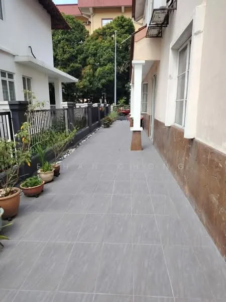 Exterior type: linked terrace house; features: grey tiled walkway, potted plants along the pathway, fenced boundary, manicured landscaping, side entrance to the house, decorative stone border, outdoor lighting fixtures, greenery in the background; style: modern.