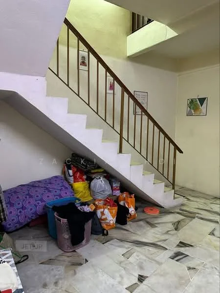 Room features: staircase with wooden railing, marble flooring with mixed patterns, white painted walls, decorative wall art, storage area under stairs, various bags and items on the floor, purple patterned cushion, laundry basket.