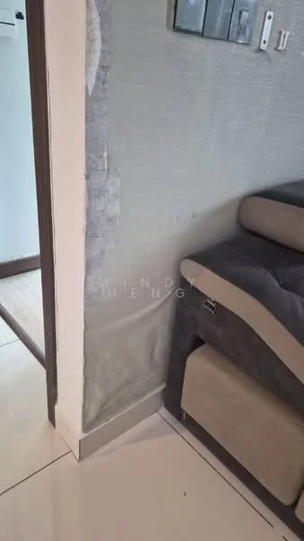 Room features: grey upholstered sofa, cream wall, tile flooring, corner of wall with peeling paint, light switch, door frame, visible edge of another room; style: modern.