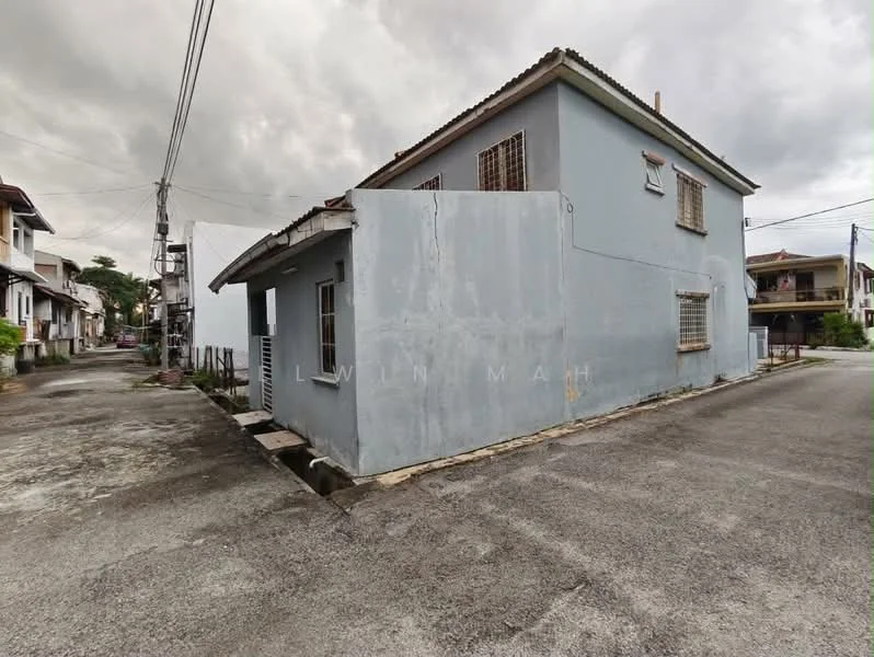 Exterior type: detached bungalow; features: grey painted facade, single-storey, flat roof, corner lot, visible windows with metal grilles, concrete pathway, surrounded by residential buildings, adjacent to street; style: traditional.