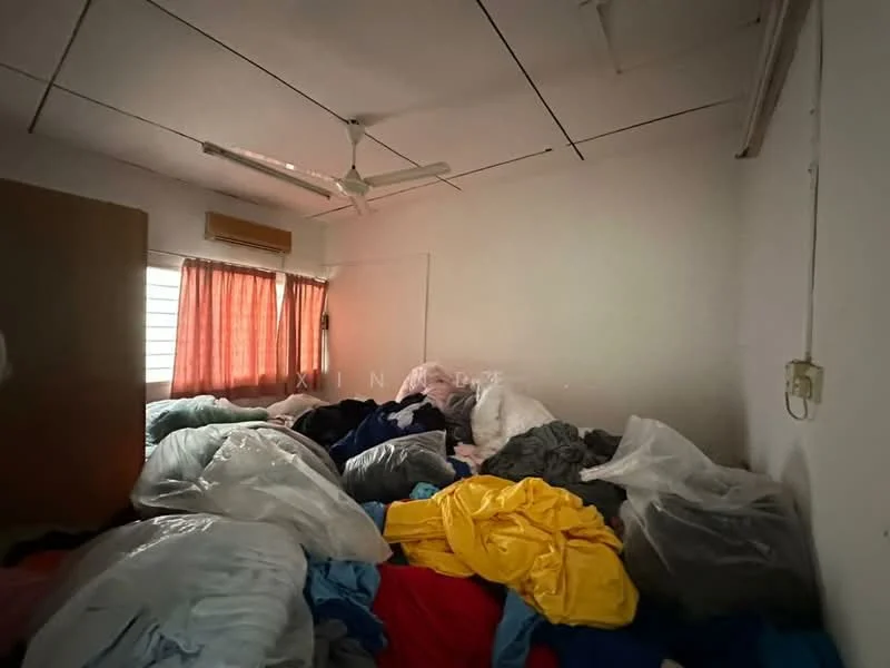 Room features: white painted walls, ceiling fan, window with sheer curtains, multiple piles of bedding, wooden wardrobe, light-colored flooring.