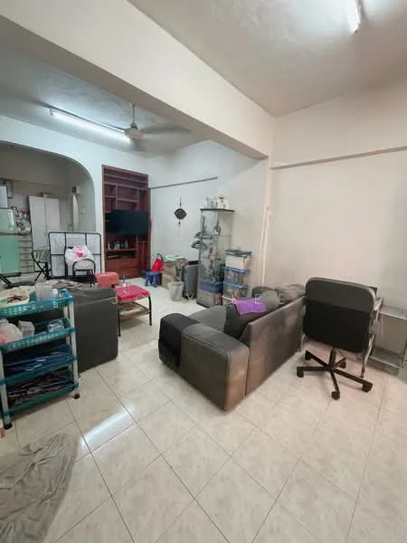Living features: grey fabric sofa, coffee table, TV console, wall-mounted TV, floor tiles, ceiling fan, light fixture, open shelving unit, decorative items on shelves, area rug, office chair, stacked cushions. Room features: white painted walls, light-colored ceiling, archway leading to another room, various household items scattered.