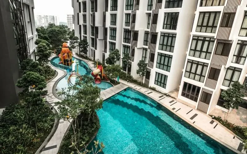 Exterior type: high-rise condominium; features: swimming pool with curved design, children's playground with slides, manicured landscaping with trees, stone-paved walkway, pool deck with loungers, water features in pool, surrounding greenery, modern architectural facade; style: modern.