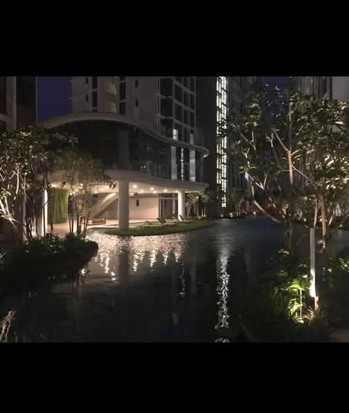 Exterior type: high-rise condominium; features: water feature with reflective surface, landscaped garden with trees, ambient lighting along pathways, modern architectural design, covered outdoor seating area, swimming pool visible in the background, glass facade of the building, manicured greenery; style: modern.