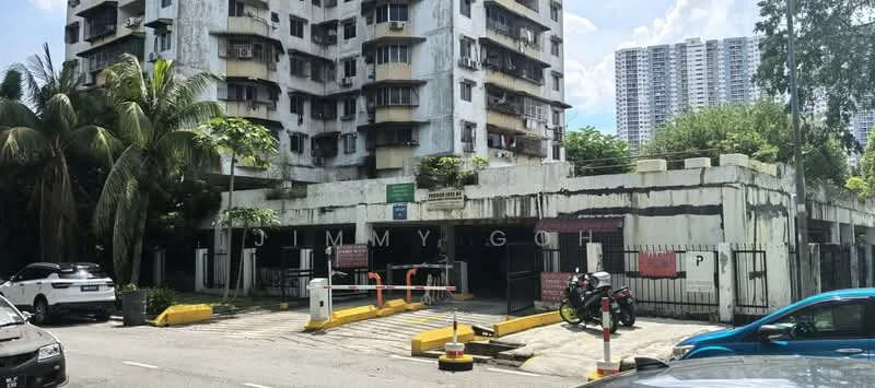 Exterior type: low-rise apartment block; features: white painted facade, balconies with metal railings, ground-level parking area, security gate at entrance, surrounded by palm trees, multiple storeys, visible signage, urban context with nearby high-rise buildings; style: traditional.