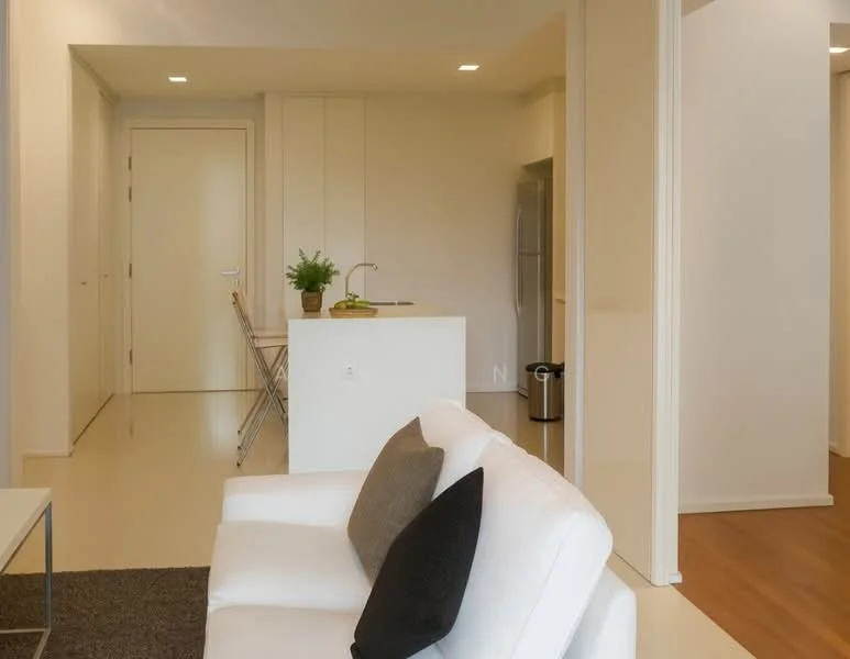 Living features: white fabric sofa, black accent pillows, coffee table, area rug, recessed downlights, light-colored walls, laminate flooring, open layout to kitchen, floor-to-ceiling door, plant in ceramic pot; style: modern. Kitchen features: kitchen island with seating, stainless-steel fridge, white cabinetry, countertop, bar stools, recessed lighting; style: modern. Room features: light-colored walls, laminate flooring, doorway leading to hallway.