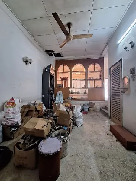 Room features: concrete flooring, white painted walls, ceiling fan, wall-mounted light fixtures, various cardboard boxes, plastic bags, metal containers, open doorway, arched windows, cluttered space.