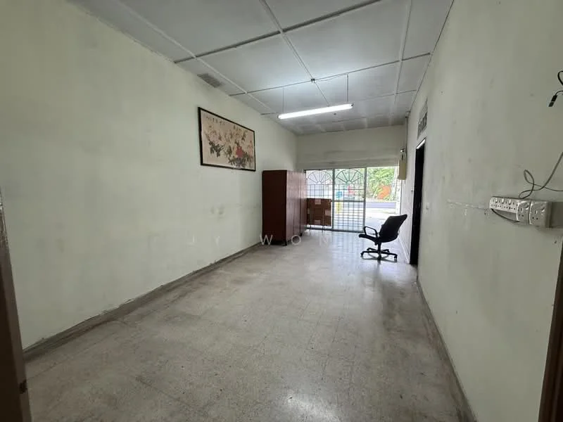 Room features: white painted walls, concrete flooring, ceiling lights, window with security grille, wooden cabinet, office chair, framed artwork on wall.