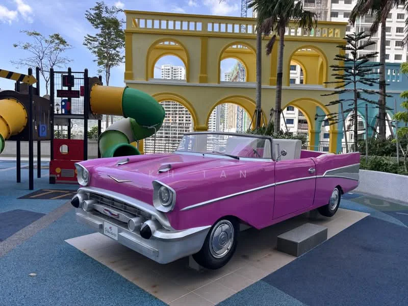 Exterior type: landscape garden; features: playground equipment, colorful slides, pink vintage car, manicured landscaping, paved walkway, surrounding greenery, decorative arches, urban setting; style: modern.