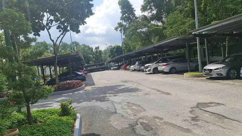 Exterior type: parking deck; features: covered parking spaces, asphalt driveway, landscaped greenery, trees providing shade, marked parking bays, surrounding flower beds, multiple vehicles parked, partially cloudy sky; style: modern.