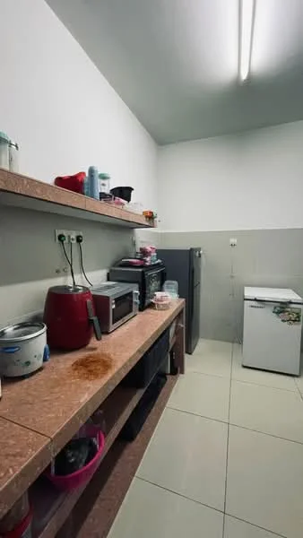 Laundry features: white walls, grey tiled flooring, shelves with storage containers, red kettle, microwave, stainless-steel fridge, white chest freezer, countertop with pink storage bins, multiple bottles of cleaning supplies, light fixtures on ceiling.