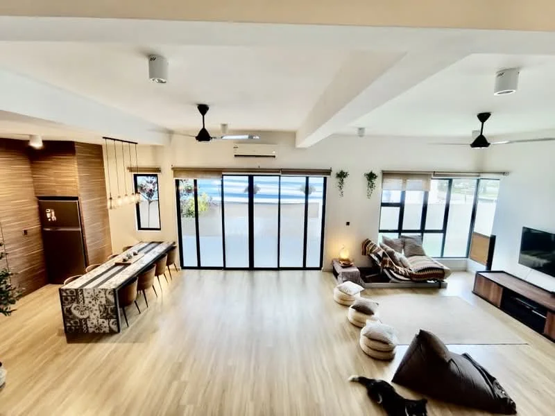 Living features: light wood flooring, exposed beams on ceiling, 5-blade ceiling fan, wall-mounted TV, large sliding glass doors, floor-to-ceiling windows, L-shape sectional sofa in beige, coffee table, decorative cushions, area rug, wall-mounted shelves, potted plants, recessed downlights; style: modern; view: garden. Dining features: long dining table with patterned surface, upholstered dining chairs, pendant lighting above table, open shelving, decorative wall paneling; style: modern; view: garden.