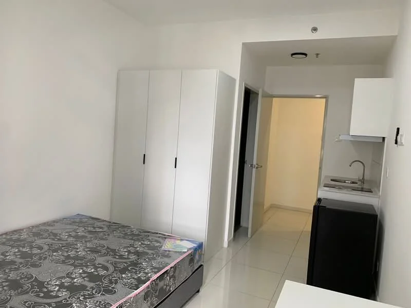 Bedroom features: queen-size bed with patterned bedding, white wardrobe with sliding doors, kitchenette with sink, black refrigerator, white tiled flooring, plain white walls, ceiling light fixture, doorway leading to hallway; style: modern.