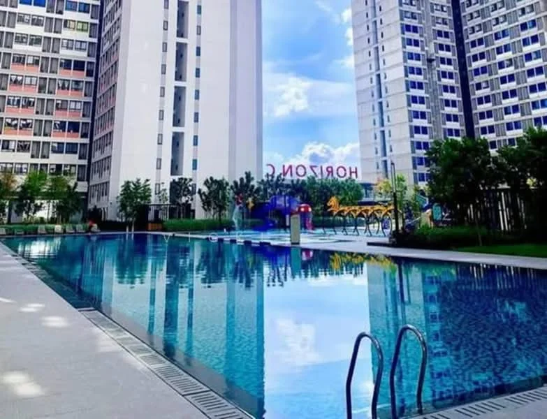 Exterior type: high-rise condominium; features: infinity pool, pool deck with loungers, surrounded by landscaped gardens, children's playground visible, modern architecture, glass curtain wall facade, manicured lawn, paved walkway; style: modern.