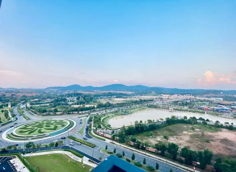 Exterior features: city skyline view, landscaped roundabout, river visible, mountainous background, open sky, greenery surrounding the area, road network, urban development in the distance; style: modern.