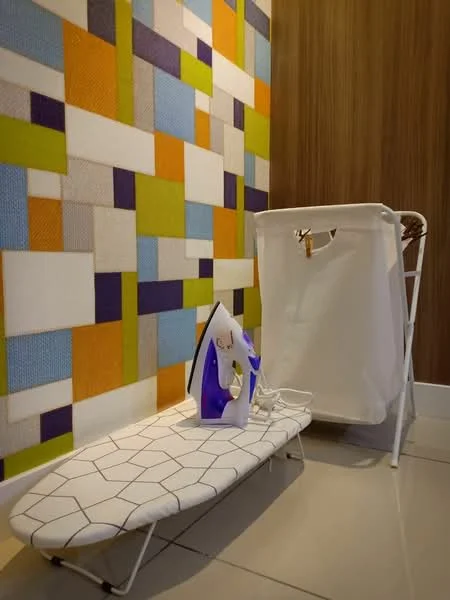 Laundry features: ironing board with geometric pattern, purple and white iron, white laundry basket, textured wall with colorful geometric design, cream tiled flooring, wood paneling on one wall; style: modern.