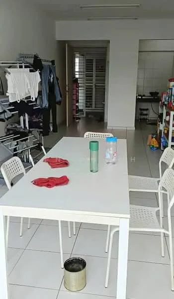 Dining features: white rectangular dining table, 4 white plastic dining chairs, red towels on the table, ceramic water bottle, plastic bottle, tile flooring, bright lighting, open layout, clothes drying rack, laundry area visible in background. Kitchen features: kitchen cabinets, stainless-steel sink, cooking stove, tile backsplash, open shelving, kitchen utensils visible.