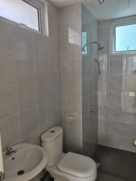 Bathroom features: white ceramic toilet, single-sink vanity with white cabinet, chrome basin mixer faucet, walk-in shower with glass enclosure, rain shower head, grey tile flooring, light grey wall tiles, small window for natural light; style: modern.