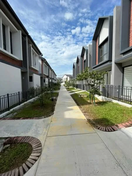 Exterior type: linked terrace house; features: manicured lawn, paved walkway, landscaped garden beds, two-storey buildings, modern facade with grey and white elements, fenced front yards, trees planted along the pathway, clear blue sky, sidewalks on both sides of the pathway; style: modern.
