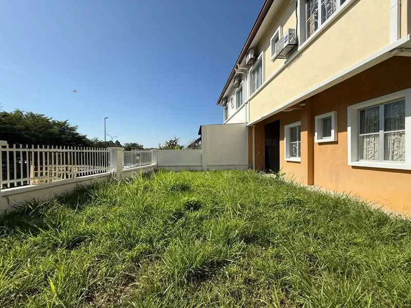 Exterior type: semi-detached house; features: yellow painted facade, white window frames, manicured lawn, fenced yard, two-storey structure, visible air conditioning units, garden area with overgrown grass; style: modern.