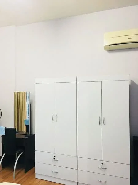 Room features: white wardrobe with drawers, black desk chair, wooden flooring, mirror on desk, wall-mounted air conditioning unit, light-colored walls, curtains, desk.