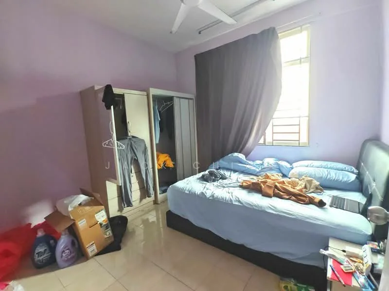 Bedroom features: purple painted walls, tile flooring, queen-size bed with grey upholstered headboard, bedding in light blue, ceiling fan, built-in wardrobe with sliding doors, clothes hanging on wardrobe, laptop on bed, cardboard boxes, window with curtain, decorative throw on bed.