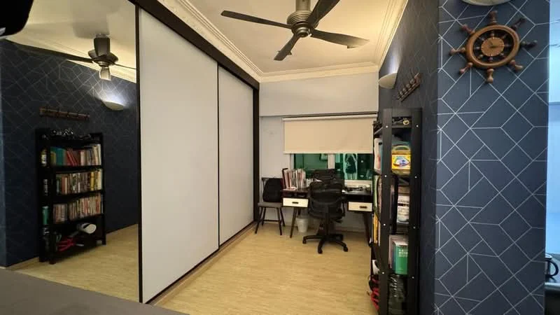 Study features: blue accent wall with geometric pattern, white sliding doors, wooden flooring, 2 ceiling fans, built-in shelving unit, desk with 2 office chairs, window with roller blinds, decorative wall clock; style: modern.