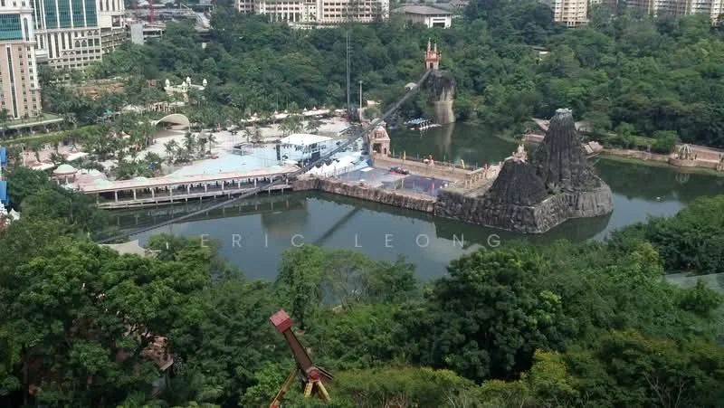 Exterior features: lush greenery, water body, theme park structures, rock formations, walkways, surrounding high-rise buildings, urban landscape, park area; style: modern.