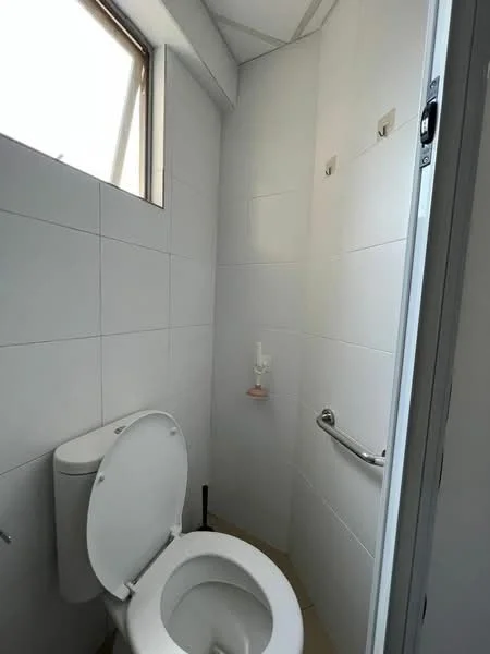Bathroom features: white tiled walls, light beige tiled flooring, one-piece toilet, grab bar, small window for natural light, wall-mounted toilet paper holder, soap dispenser, corner shower area; style: modern.