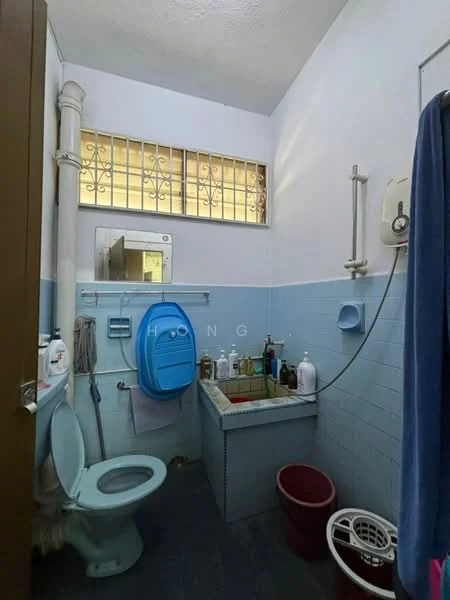 Bathroom features: toilet, blue ceramic toilet, sink with cabinet, mirror above sink, shower head, wall-mounted water heater, blue tiled walls, grey floor tiles, window with metal grille, storage shelf, waste bin.