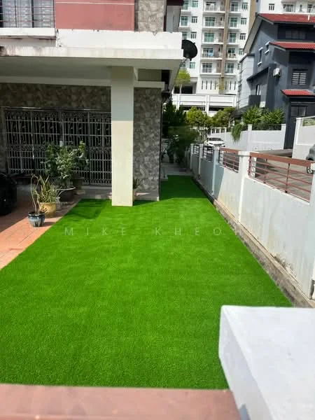 Exterior features: artificial grass lawn, stone cladding on wall, paved walkway, fenced perimeter, mature plants, residential building in background; style: modern.