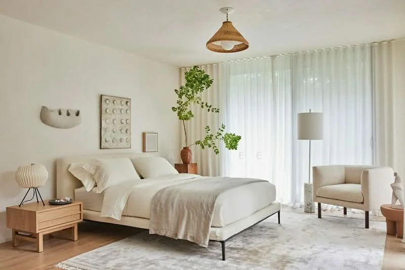 Bedroom features: queen-size bed with white bedding, upholstered headboard, wooden bedside table, table lamp with fabric shade, light-colored area rug, large windows with sheer curtains, potted plant, accent chair in light fabric, wooden flooring, pendant light fixture; style: minimalist; view: garden.