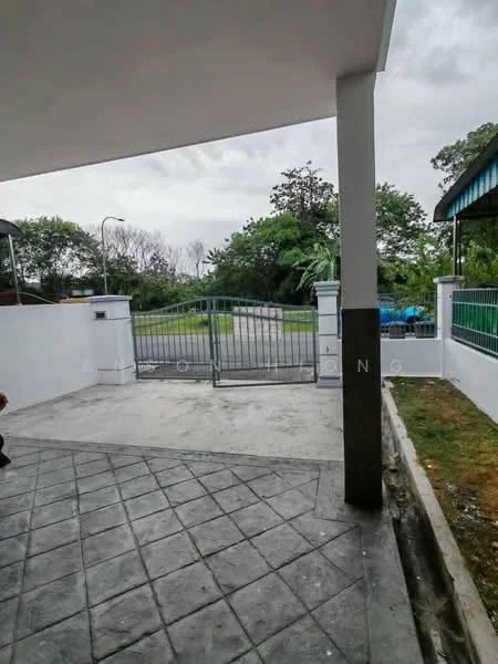 Exterior features: paved driveway, metal gate, white painted fence, green grass, surrounding trees, concrete wall, grey cloudy sky; style: modern.