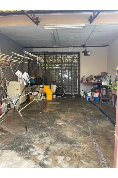 Room features: concrete flooring, metal security grille door, clothes drying rack, storage shelves, various household items, yellow plastic bucket, wall-mounted light fixture, exposed ceiling, utility area.