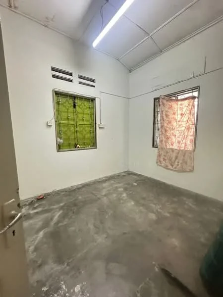 Room features: plain white walls, concrete flooring, single window with green grille, curtains on window, exposed ceiling, fluorescent lighting, no visible built-in storage, minimal decor; style: minimalist.
