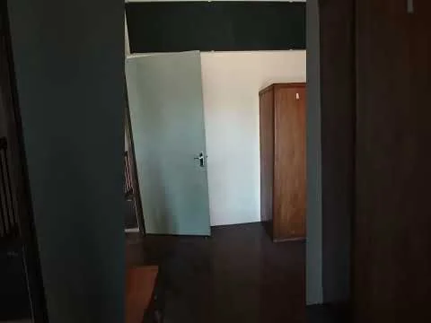 Room features: wooden flooring, green accent wall, light-colored door, wooden wardrobe, neutral wall color, door frame, visible hallway, ceiling.