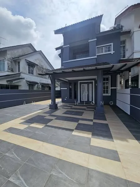 Exterior type: semi-detached house; features: grey painted facade, flat roof with overhang, covered porch area, paved driveway with alternating grey and beige tiles, white window frames, double doors at entrance, surrounding wall with horizontal stripes, two-storey structure, visible neighboring houses, manicured landscaping; style: modern.