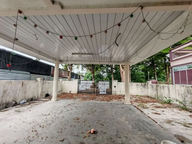 Exterior features: covered outdoor area, decorative ceiling with beams, concrete flooring, perimeter wall, gated entrance, surrounded by greenery, overhead string lights, dirt and leaves on the ground.