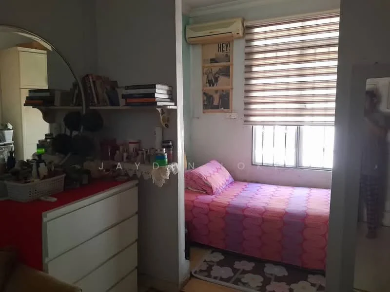 Bedroom features: single bed with pink and purple patterned bedding, built-in wardrobe, white dresser with multiple drawers, wall-mounted air conditioning unit, window with horizontal blinds, decorative wall art, bookshelf with stacked books, area rug with geometric pattern.