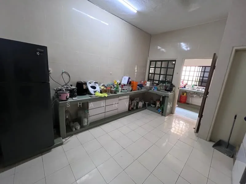 Kitchen features: white tiled walls, glossy white tile flooring, grey countertop, black refrigerator, stainless-steel sink, wall-mounted cabinets, kitchen appliances including kettle and rice cooker, multiple containers and utensils on countertop, window with grid pattern, door leading to another room.
