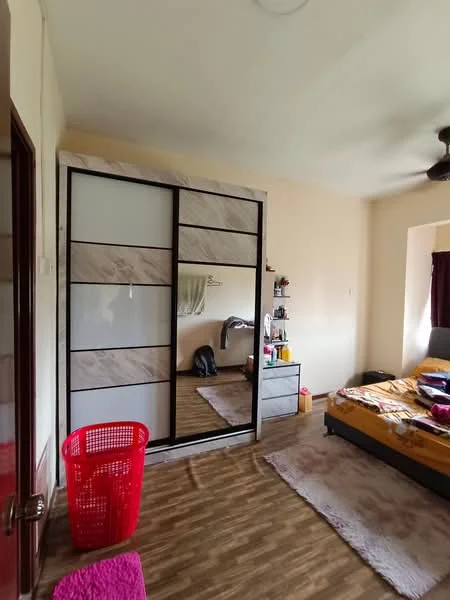 Bedroom features: queen-size bed with yellow bedding, upholstered headboard, built-in wardrobe with sliding doors, wooden flooring, ceiling fan, decorative wall mirror, pink area rug, red laundry basket, nightstand with items, window with dark curtains.