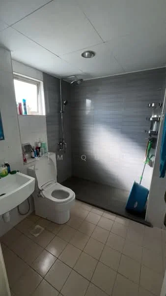 Bathroom features: white toilet, single-sink vanity with wall-mounted faucet, shower area with glass partition, chrome shower head, grey tiled walls, beige floor tiles, mirror above sink, various toiletries on sink, window for natural light; style: modern.