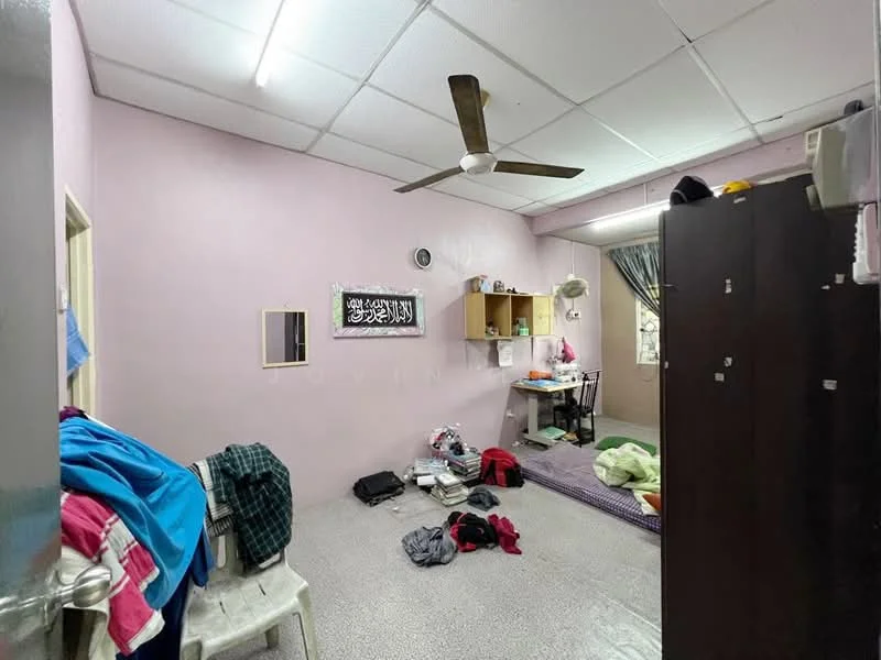 Room features: pink painted walls, ceiling fan, polished concrete flooring, single bed, study desk, wooden wardrobe, clothes on the floor, plastic chair, window with curtain.
