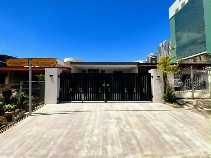 Exterior type: detached bungalow; features: black metal gate, concrete driveway, surrounding fence, landscaped garden, signage on the gate, single-storey building, clear blue sky, urban context with nearby buildings; style: modern.